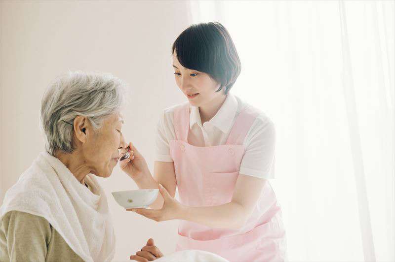 看護師の女性が食事を高齢女性の口に運んでいる姿